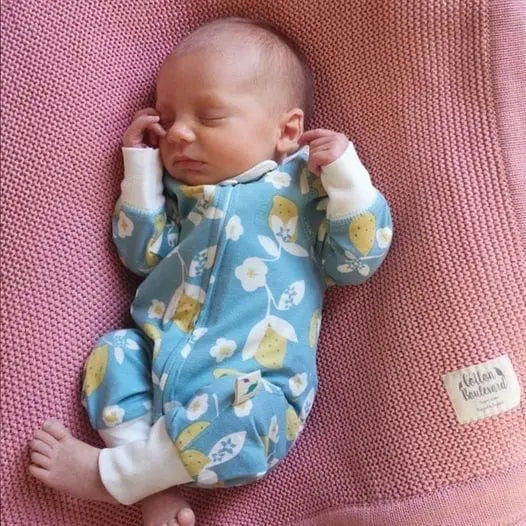 iny baby lying on a pink organic cotton blanket, wearing a soft lemon romper made from GOTS certified organic cotton.